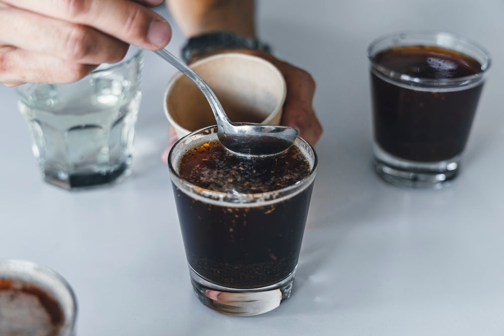 グラスに満たしたコーヒーの表面をスプーンで崩し、香りを確かめるカッピングの様子
